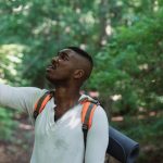Fear Of Failure - African American male with backpack standing in forest and holding mobile phone while catching GPS signal during hike